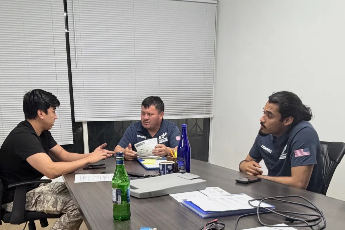Three ApexPro team members around a table reviewing printed technical documents and notes